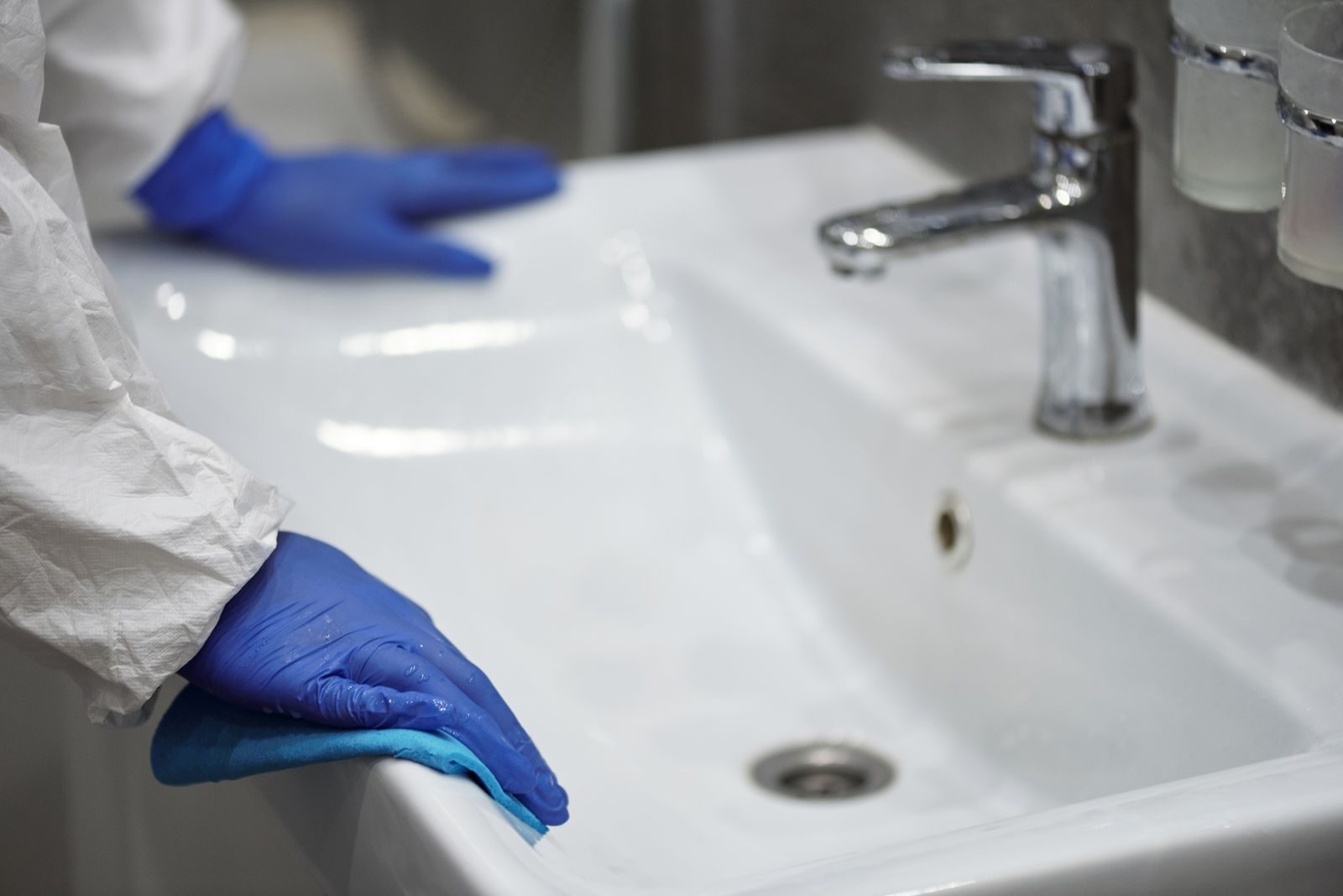 Gloved hands scrubbing a white bathroom sink